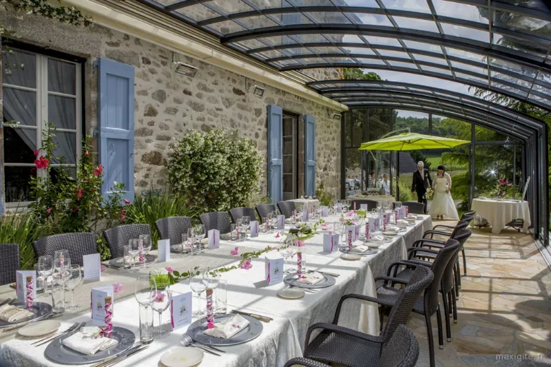 Grande table dressée sous véranda vitrée ouverte sur la campagne, décoration soignée