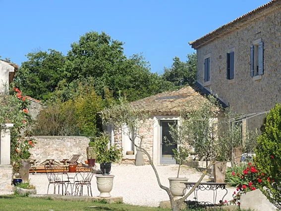 Façade en pierre du mas provençal avec piscine et jardin, ciel bleu et volets clairs