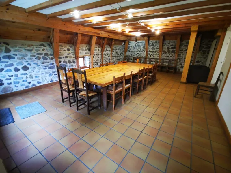 Grande salle à manger aux murs en pierre et poutres apparentes avec longue table en bois pour le groupe