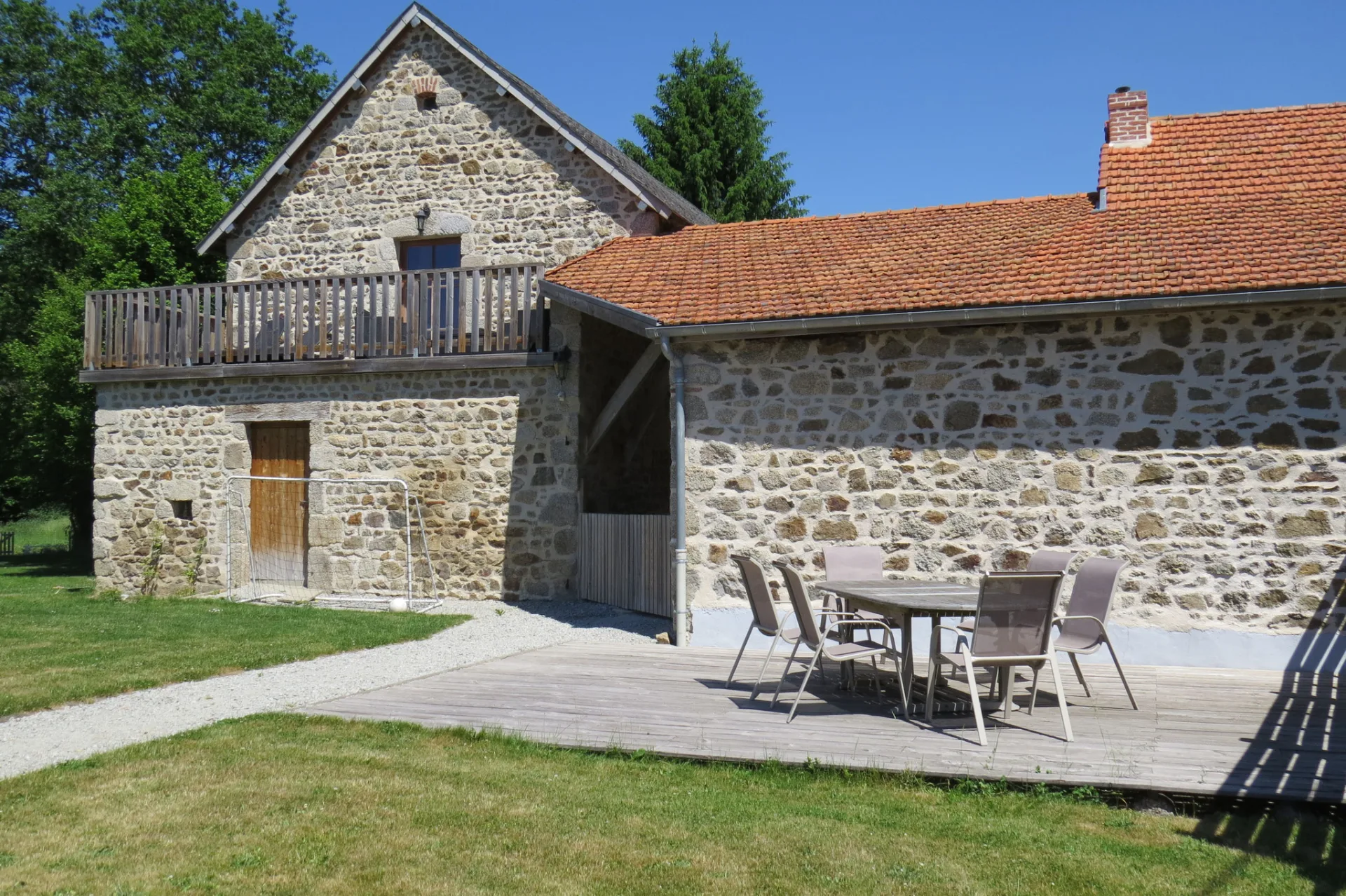 Gîte de groupe L'Élémentaire à Charensat — Façade en pierre du domaine avec grande terrasse repas et balcon en bois, capacité 25 personnes