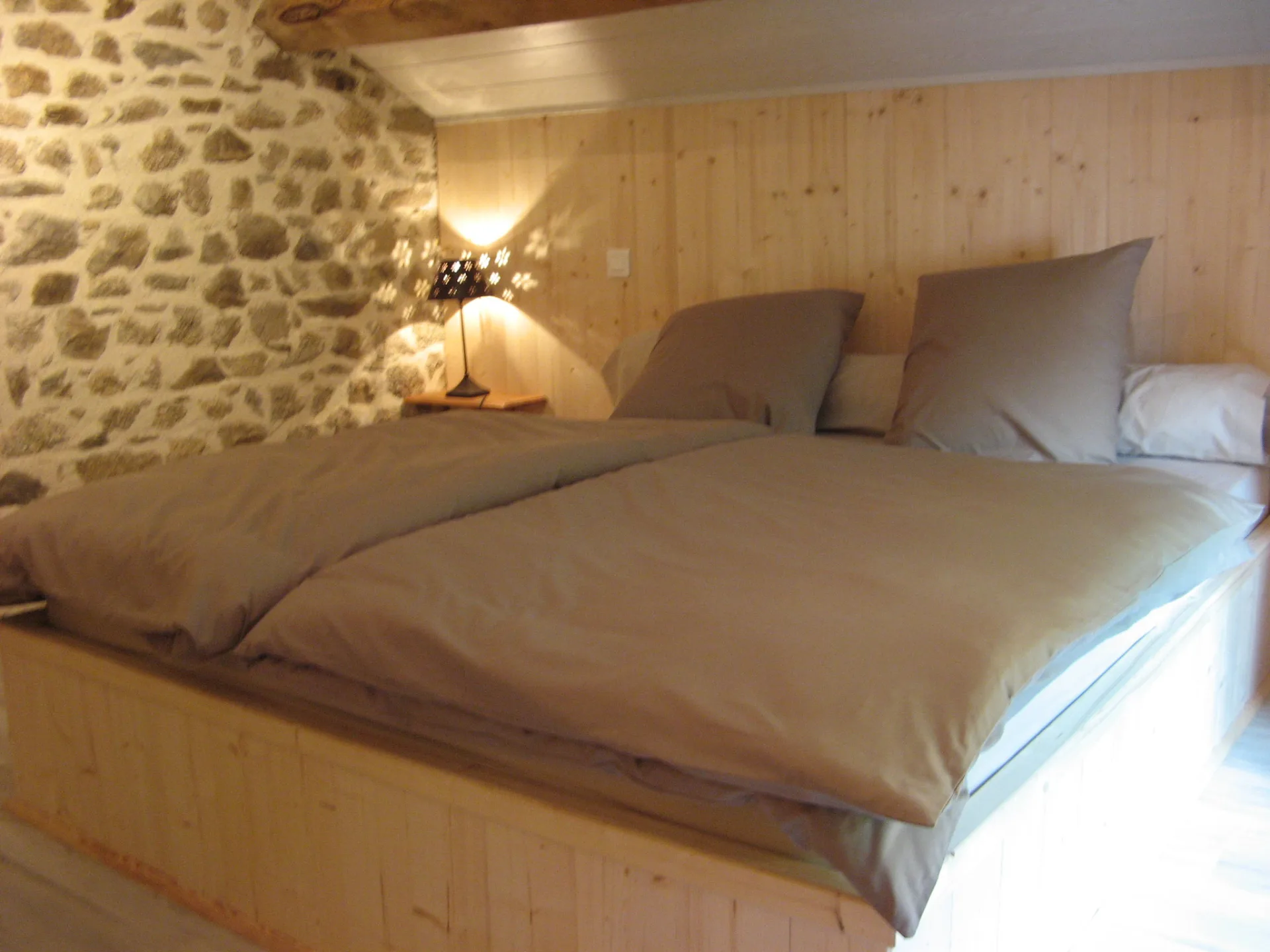 Chambre mansardée avec lit double, mur en pierre apparente et lampe de chevet
