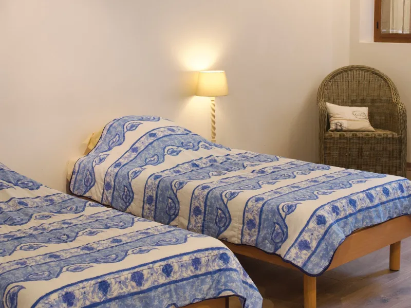 Chambre avec lits jumeaux à linge fleuri, fauteuil en osier et lampe de chevet