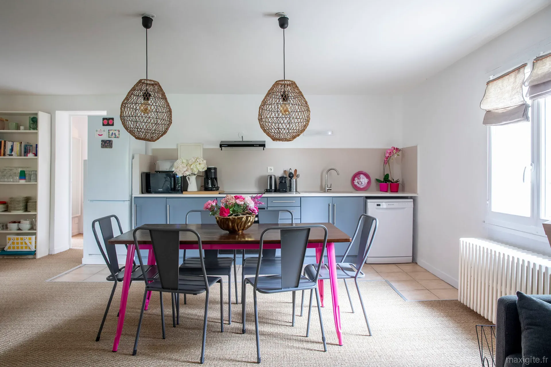 Grande cuisine ouverte avec suspensions en rotin, table à 6 chaises et mobilier coloré rose et gris
