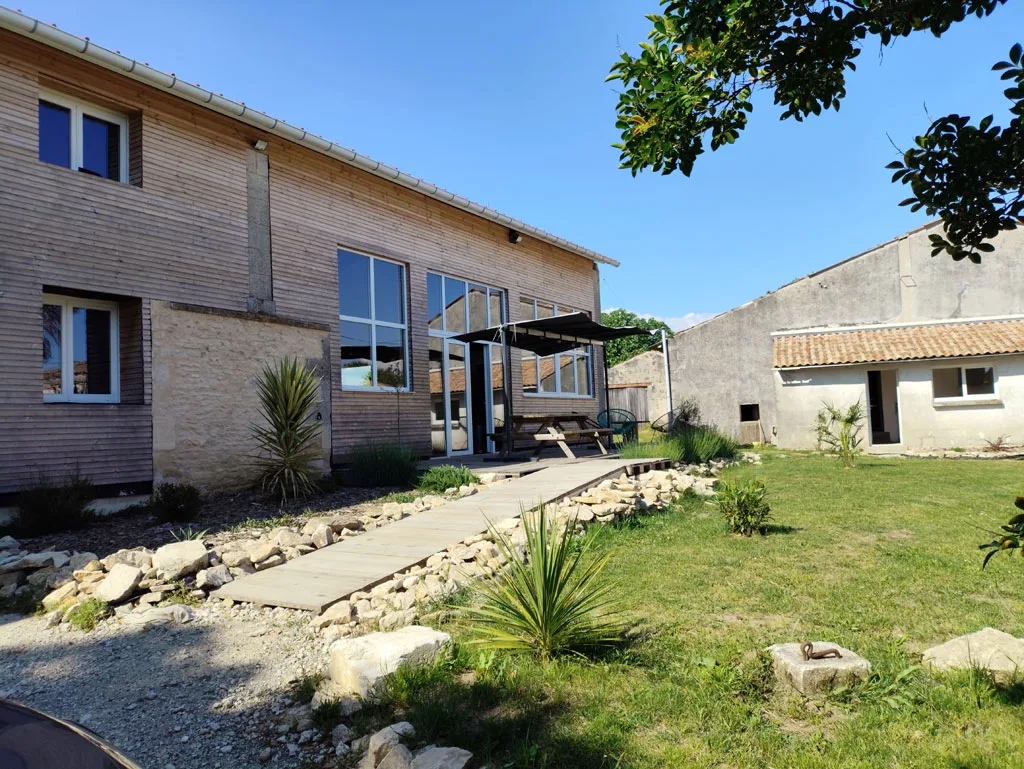 Gîte de groupe La Grange - Le Glorit à Val de Livenne — Façade en bois et pierre de la Grange, jardin arboré et allée en bois menant à l'entrée, capacité 15 personnes