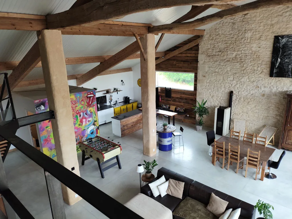 Vue depuis la mezzanine sur la grande pièce à vivre, charpente en bois et mur en pierre apparente