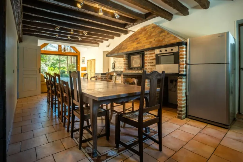 Grande salle à manger avec table en bois pour 14 convives et cuisine équipée sous poutres