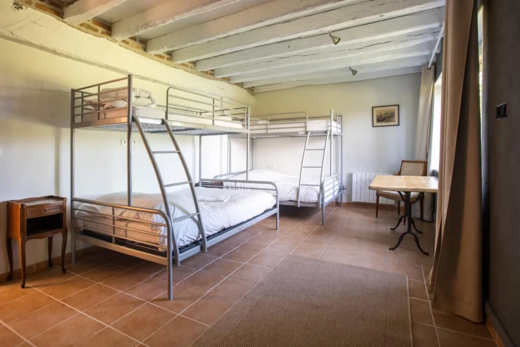 Chambre dortoir avec lits superposés en métal et poutres blanches apparentes