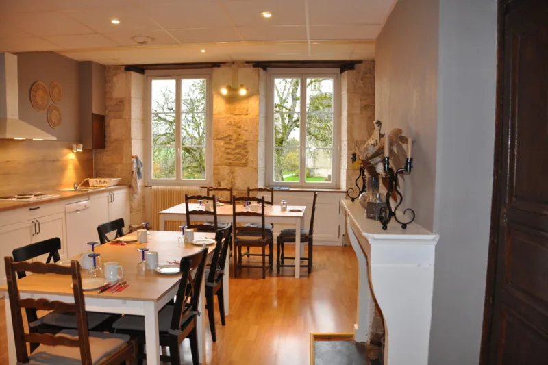 Grande cuisine équipée et salle à manger en plancher bois avec tables et murs en pierre, fenêtres sur jardin
