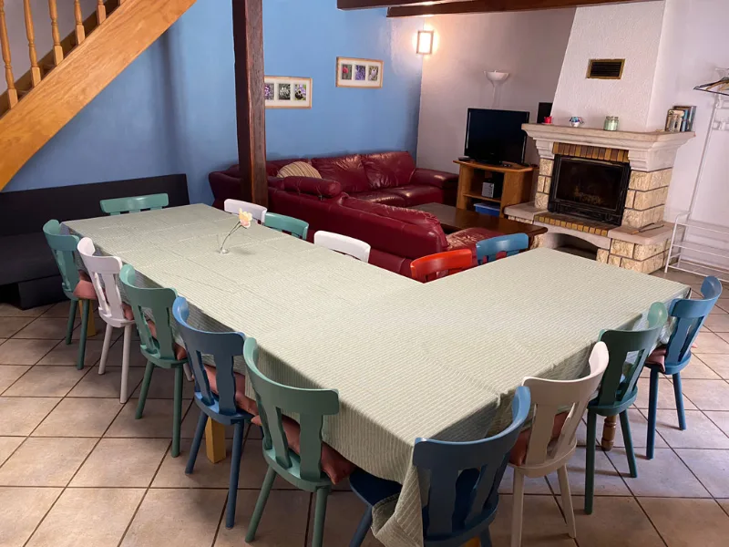 Grand salon-salle à manger du Bourdon Bleu avec grande table pour 15 convives, cheminée et canapé rouge