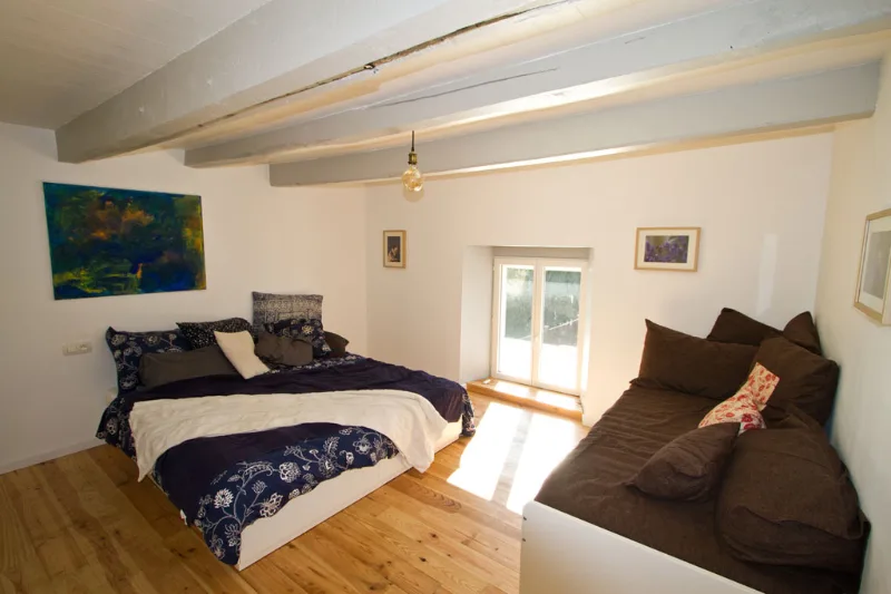Chambre lumineuse avec lit double, poutres apparentes et parquet clair, porte-fenêtre sur jardin