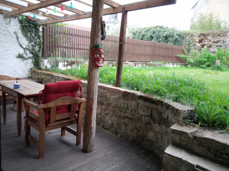 Terrasse couverte avec pergola, mobilier de jardin rouge et jardin clos verdoyant