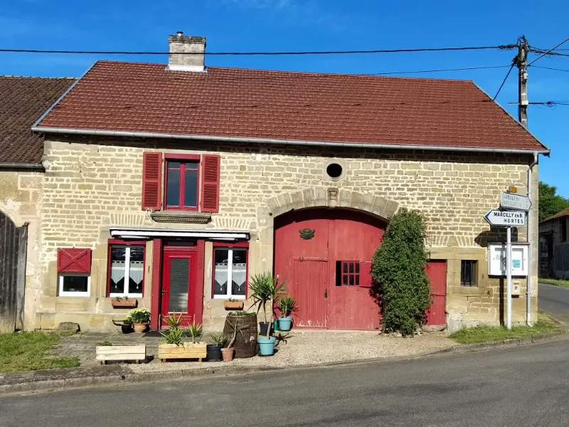 Façade en pierre de la maison Au Grain de Celles à Celles-en-Bassigny avec volets rouges et plantes en pots