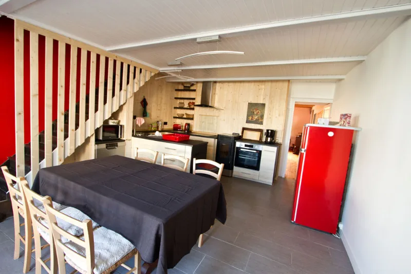 Cuisine et séjour de l'Au Grain de Celles avec frigo rouge rétro, table et lambris bois, escalier