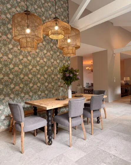 Salle à manger du gîte rénovée avec table en bois, lustres en osier et carrelage pierre