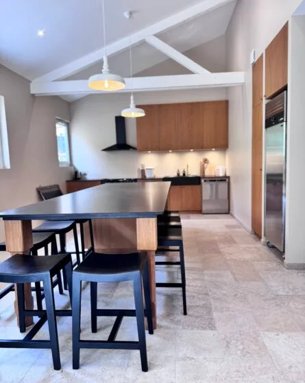 Cuisine équipée ouverte sur la salle à manger avec table et chaises noires, poutres apparentes
