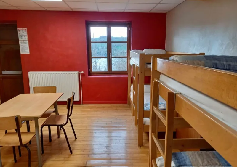 Dortoir du Centre Bellevue avec lits superposés en bois et parquet, table et chaises au centre