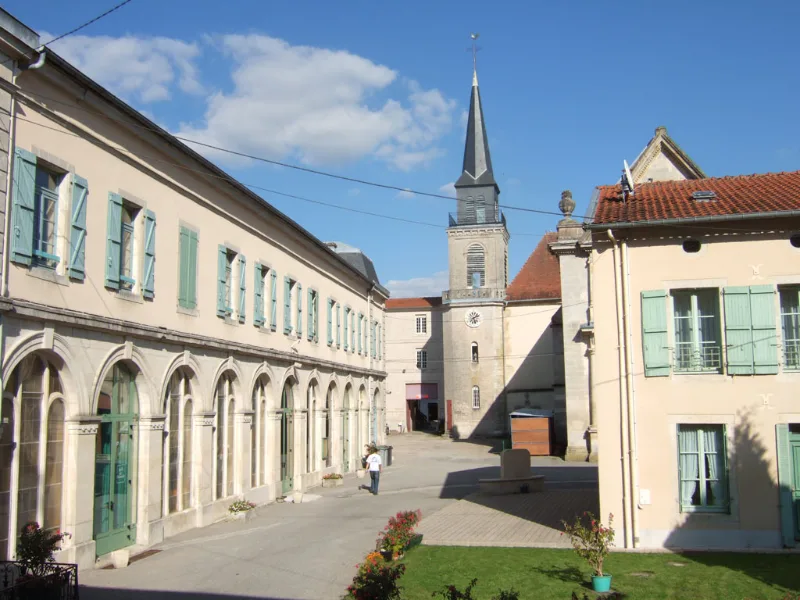 Cour intérieure du Centre d'Accueil de Benoîte-Vaux avec arcades, volets verts et clocher en arrière-plan