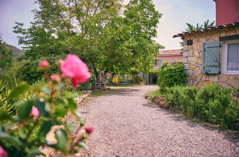 Jardin fleuri du domaine avec rosiers en fleur et bastide provençale en arrière-plan