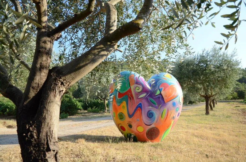 Vue du parc du Domaine Hemmitage avec sculpture artistique colorée et allée d'oliviers