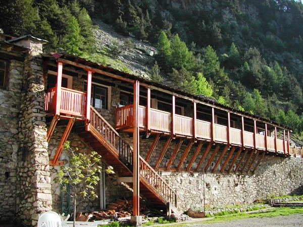 Batiment en pierre avec longue galerie en bois et escalier exterieur adosse a la montagne
