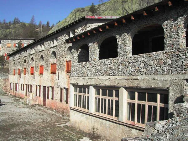 Facade en pierres du batiment principal avec arches et volets orange en montagne