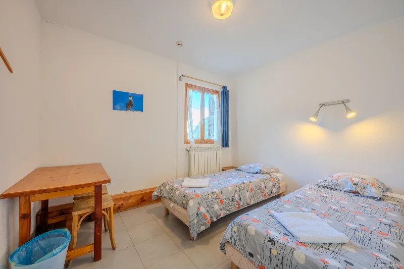 Chambre confort avec deux lits simples bureau en bois et rideaux bleus