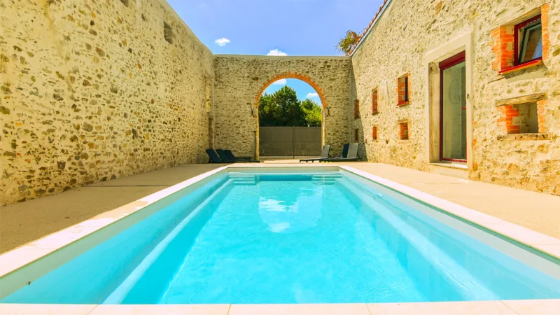 Piscine rectangulaire encadrée de murs en pierre et arche en briques