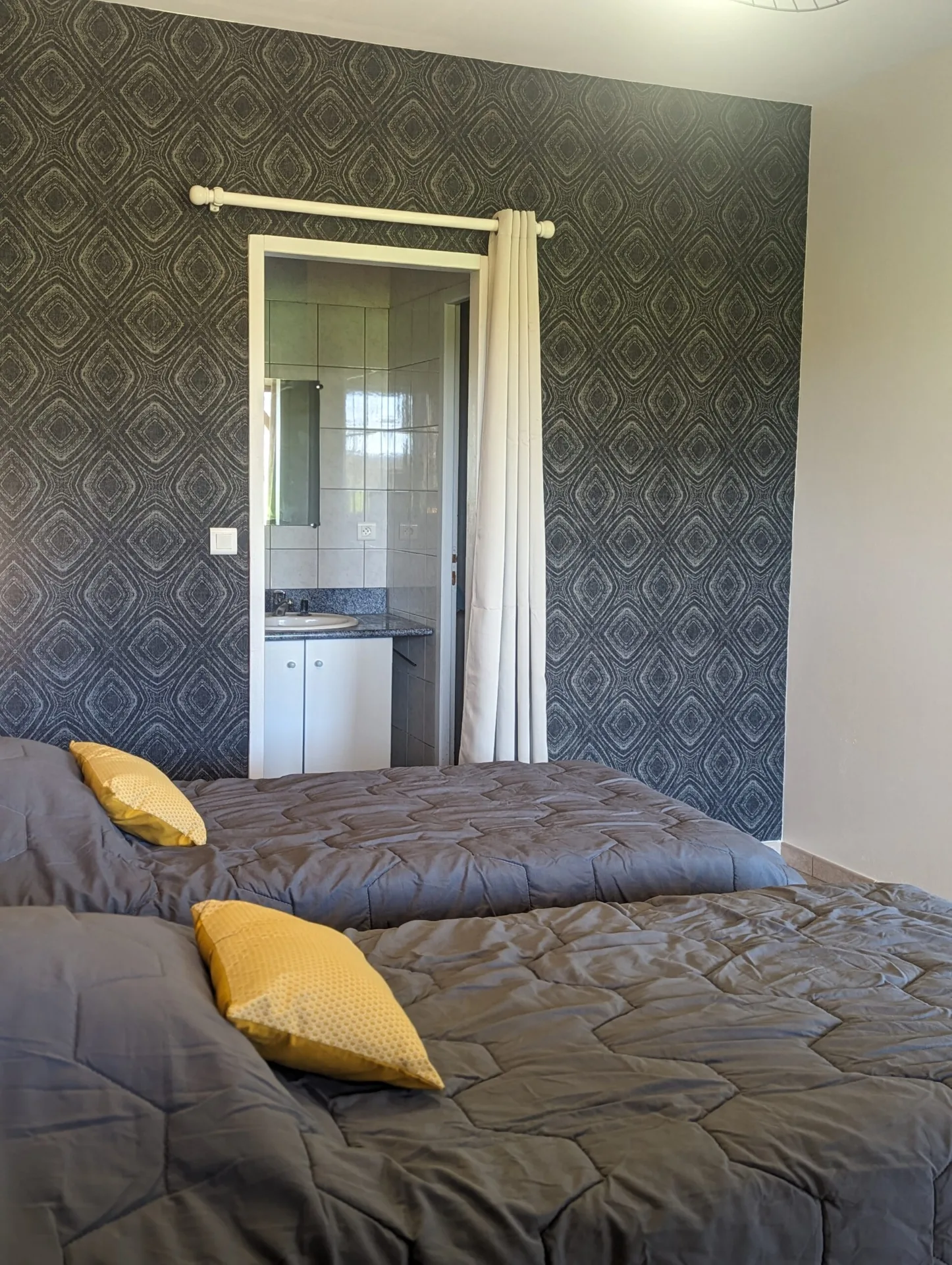 Chambre double avec papier peint geometrique, coussins jaunes et salle d eau attenante