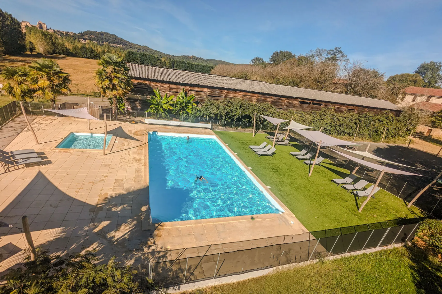 Piscine chauffee avec pataugeoire, transats et voiles d ombrage, vue sur le chateau de Beynac