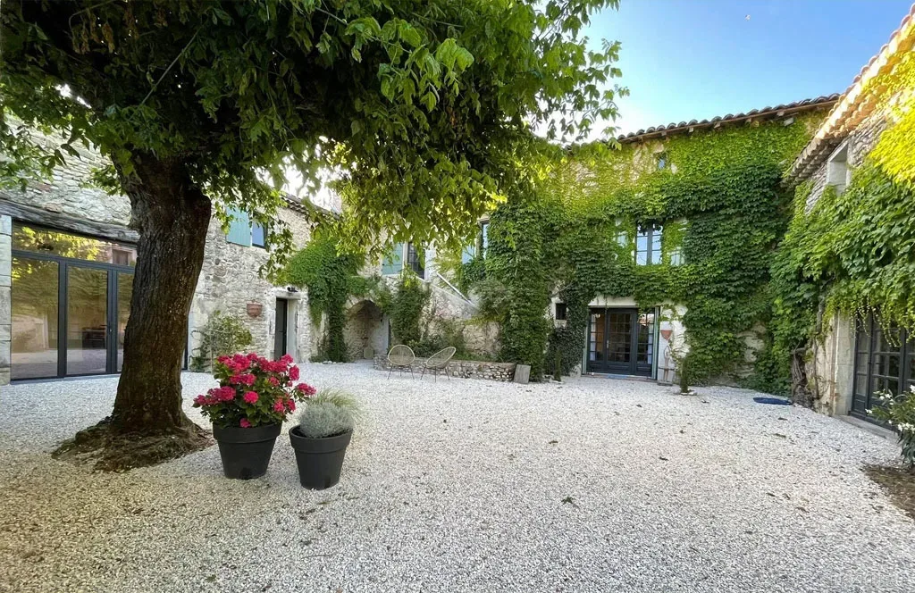 Gîte de groupe La Cour Joyeuse à La Bâtie-Rolland — Cour intérieure en gravier avec bâtiments en pierre couverts de lierre et grand arbre centenaire, capacité 16 personnes