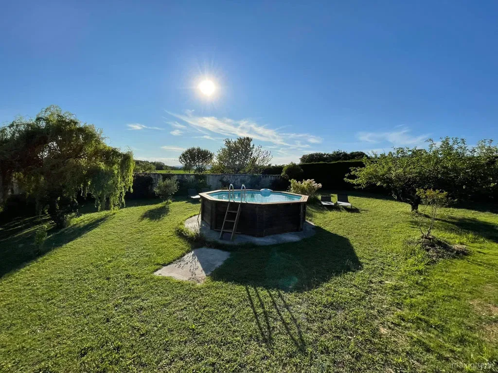 Piscine hors-sol en bois dans un jardin verdoyant avec transats et saule pleureur en arrière-plan