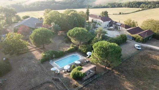 Vue aérienne du hameau avec bâtiments en pierre, piscine au sel entourée de verdure et campagne gersoise vallonnée