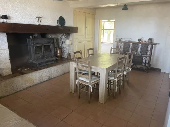 Salle à manger avec grande table en bois pour huit convives, poêle à bois dans cheminée en pierre et sol en tomettes