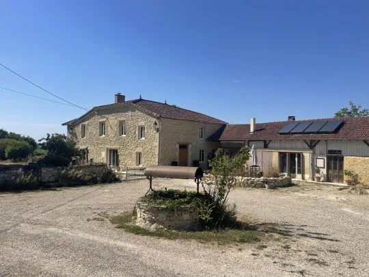 Bâtiment principal en pierre de taille avec puits ancien dans la cour, toiture en tuiles et panneaux solaires sur l'annexe