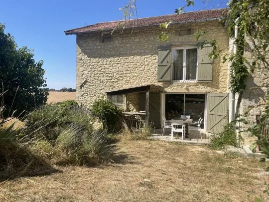 Façade en pierre du gîte l'Étable avec volets verts, petite terrasse meublée et vue dégagée sur les champs