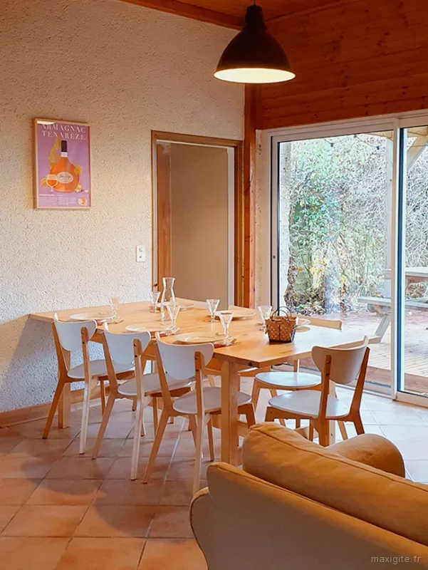 Salle à manger du gîte Ténarèze avec table dressée pour huit convives, plafond en bois, baie vitrée et affiche Armagnac
