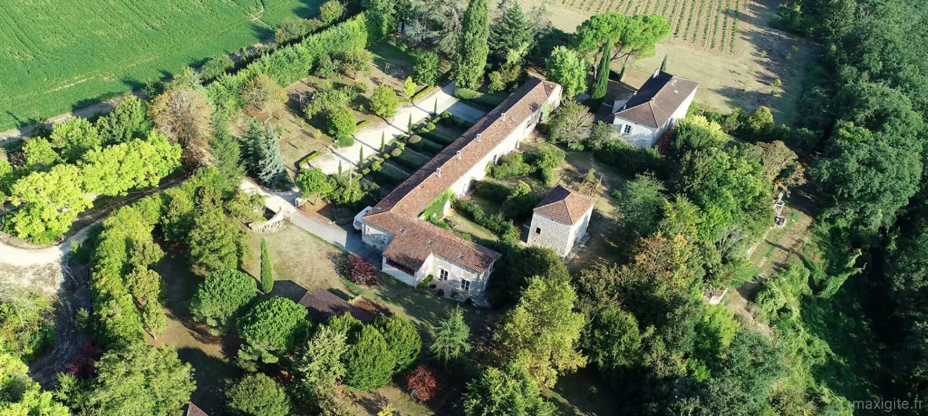 Gîte de groupe Domaine de la Brette à Condom — Vue aérienne du Domaine de la Brette avec bâtiments en pierre, toits en tuiles, cyprès et parc arboré au milieu des champs, capacité 49 personnes