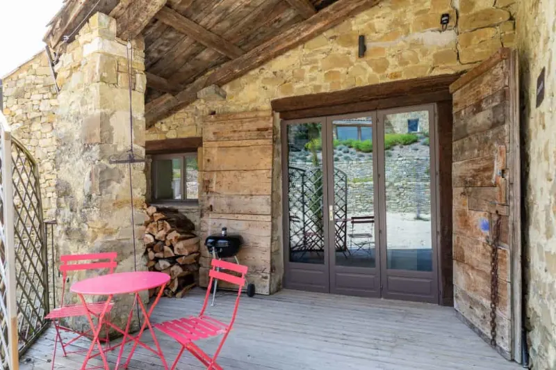 Intérieur chaleureux d'une maison en pierre avec poutres en bois, grandes fenêtres et vue sur la nature environnante