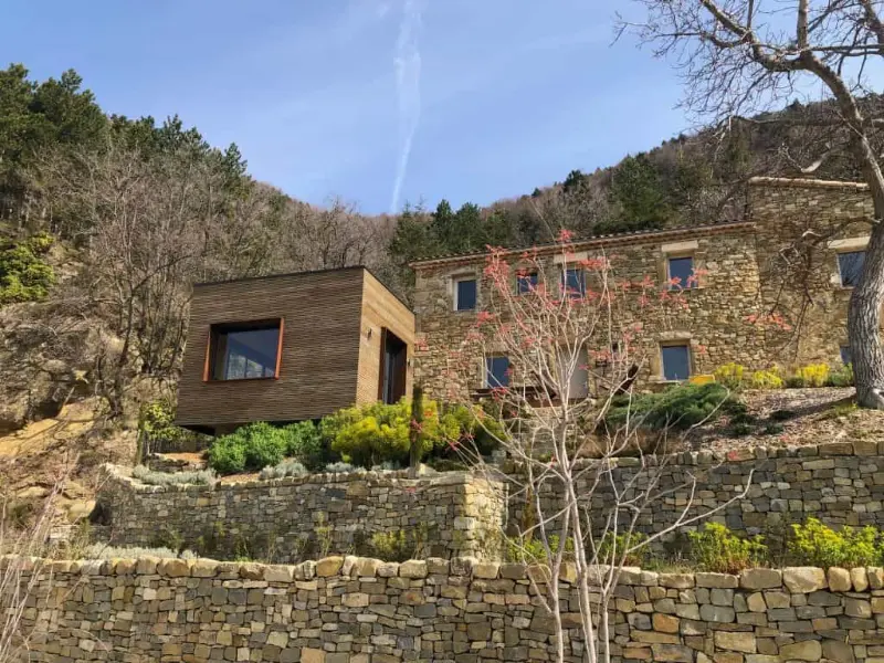 Maison La Cascade en pierre avec extension contemporaine en bois, entourée de végétation méditerranéenne et collines verdoyantes