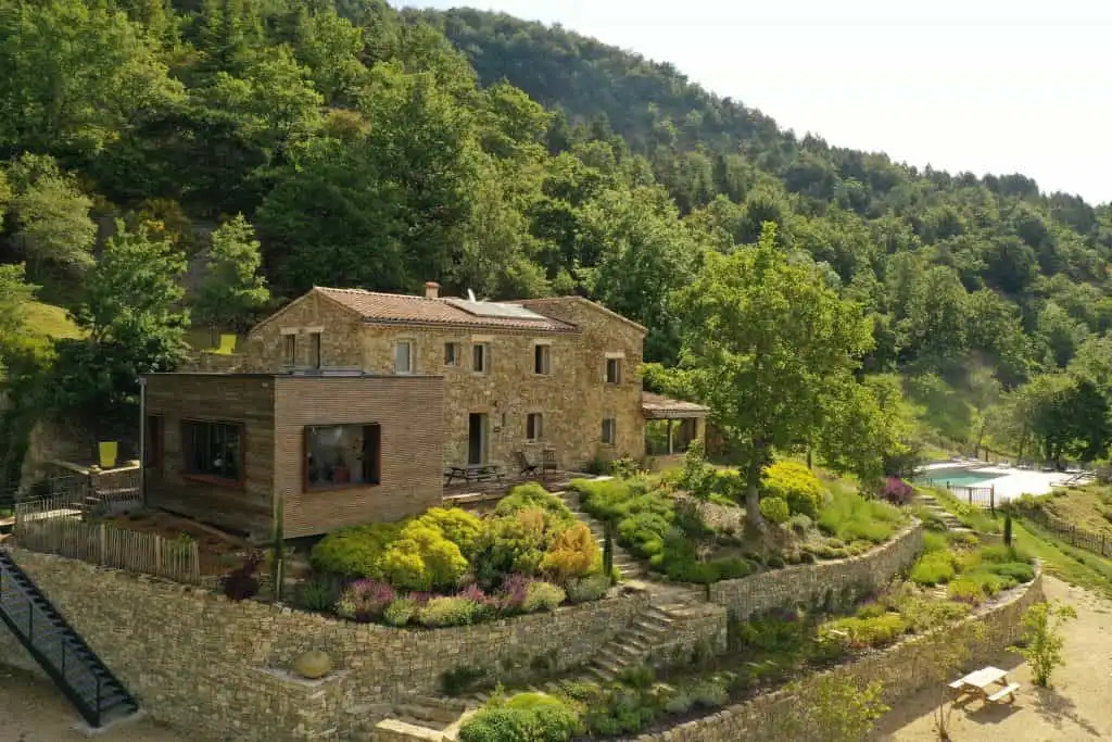 Gîte de groupe Domaine des Chauvins à Teyssières — Vue aérienne du hameau en pierre avec extension en bois, jardins en terrasses, piscine et collines boisées de Drôme Provençale, capacité 30 personnes