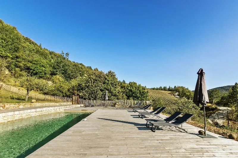 Piscine d'eau douce avec terrasse en bois de robinier, transats et parasol, vue panoramique sur la vallée et les montagnes