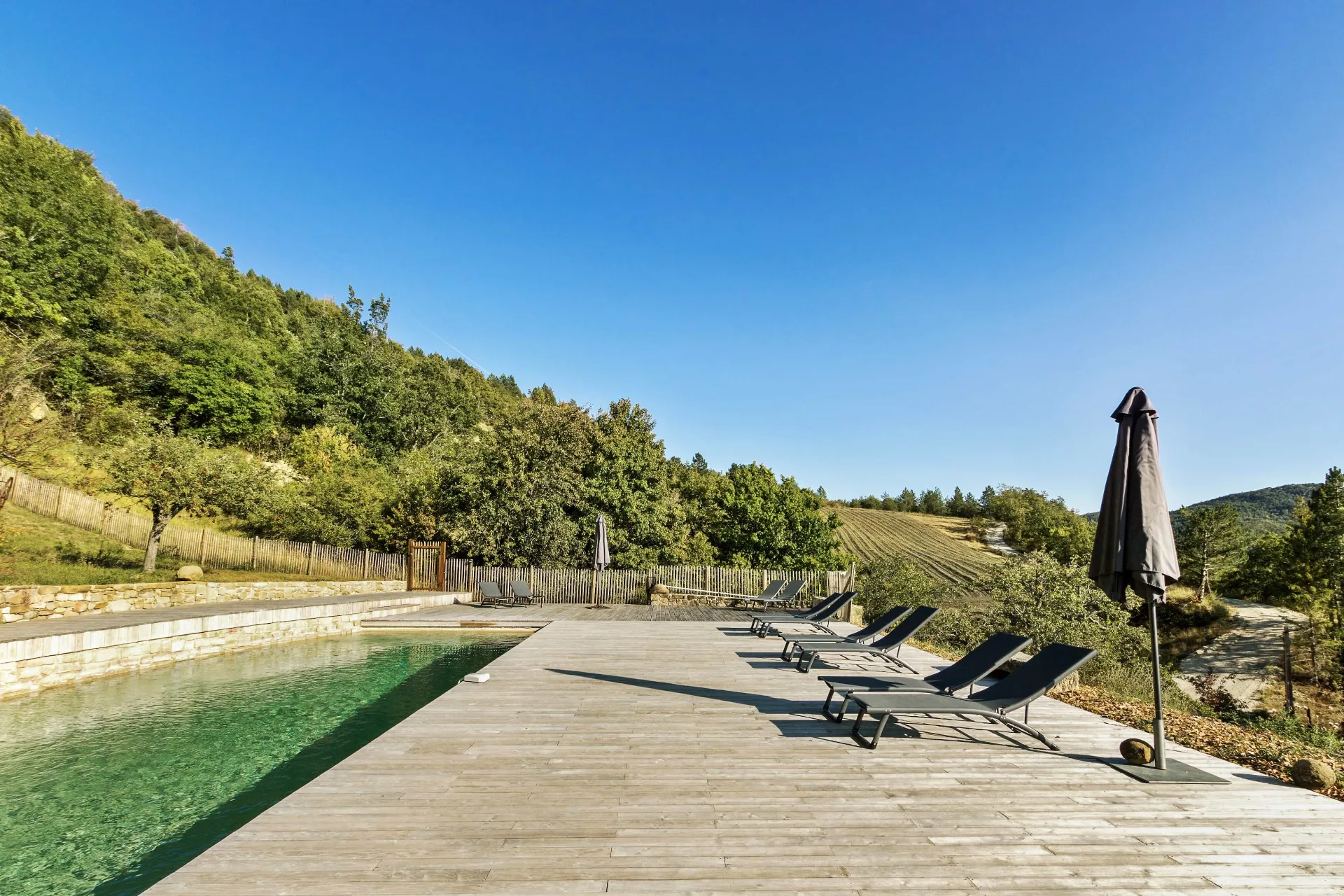 Piscine d'eau douce avec terrasse en bois de robinier, transats et parasol, vue panoramique sur la vallée et les montagnes
