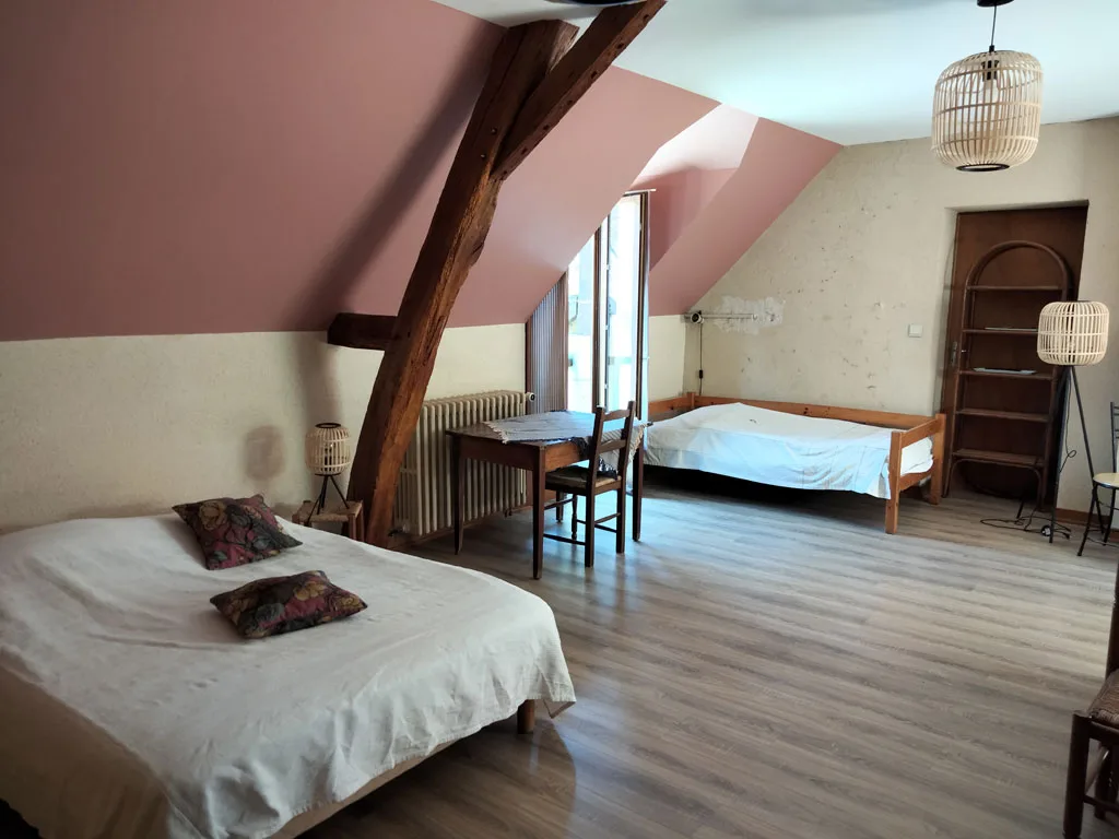 Chambre avec lit double et draps blancs sous plafond mansarde en bois clair