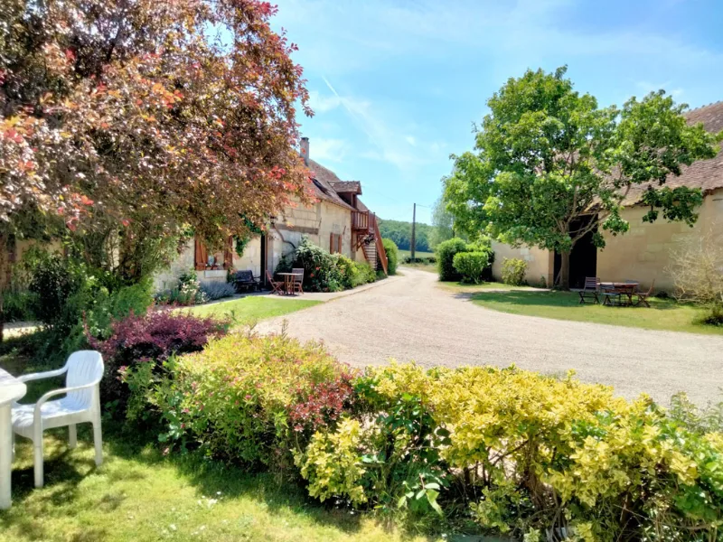 Facade principale de la ferme en pierre avec toit en tuiles entouree d'arbres et de haies fleuries