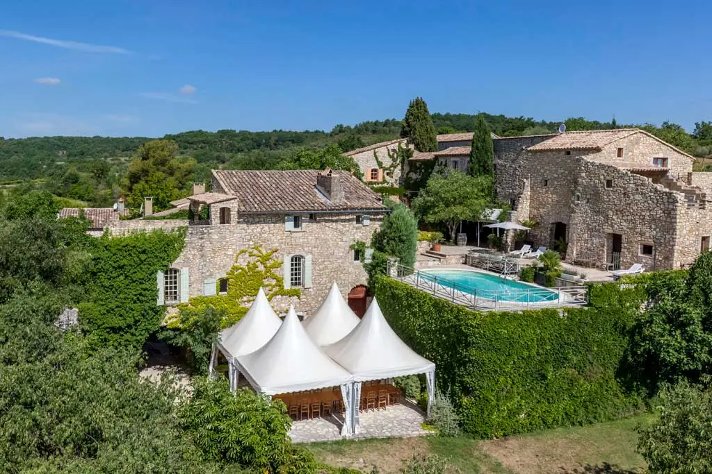 Gîte de groupe Domaine du Clos d'Hullias à Saint Christol de Rodières — Vue aérienne du domaine avec bâtiments en pierre, piscine et tentes blanches au milieu des arbres, capacité 30 personnes