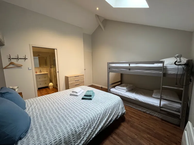 Chambre sous combles avec lit double, coussins bleus, fenêtre de toit et commode en bois clair