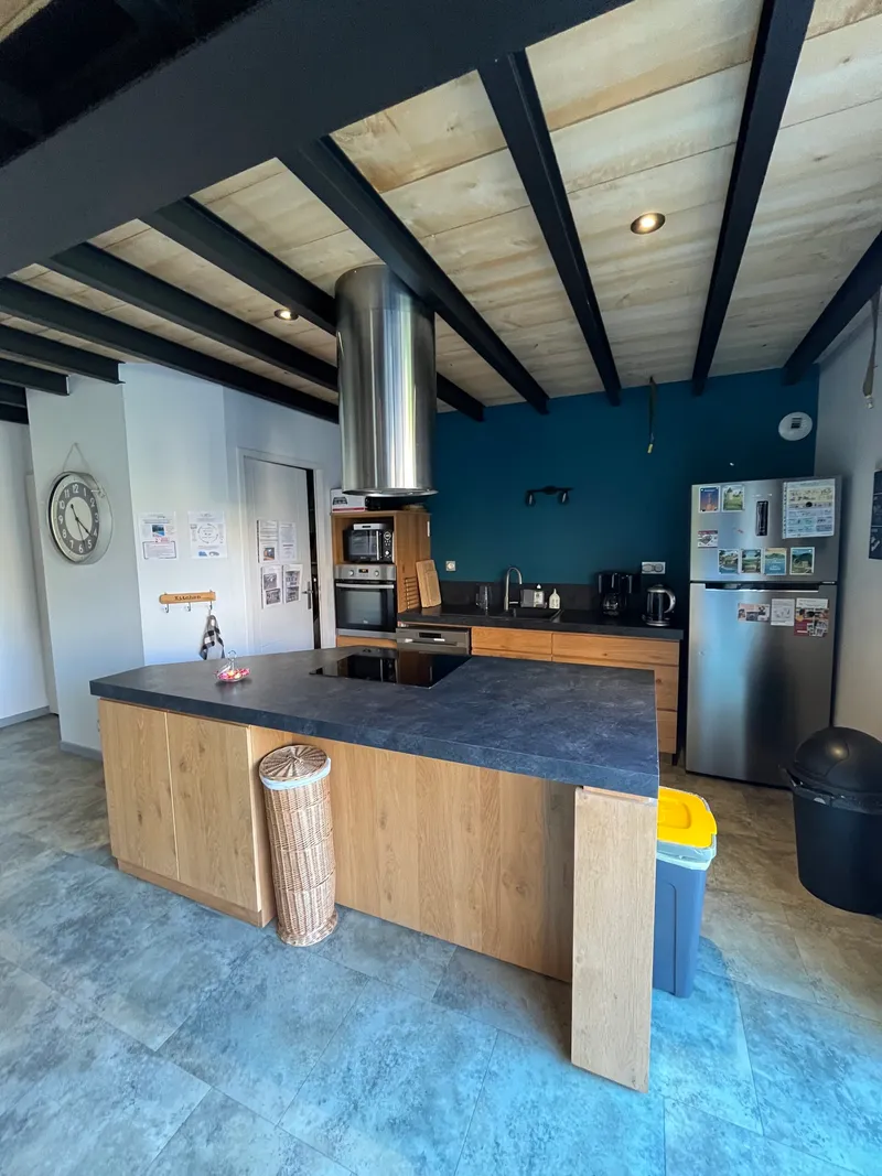 Cuisine équipée avec îlot central en bois, plan de travail sombre, hotte inox et réfrigérateur américain
