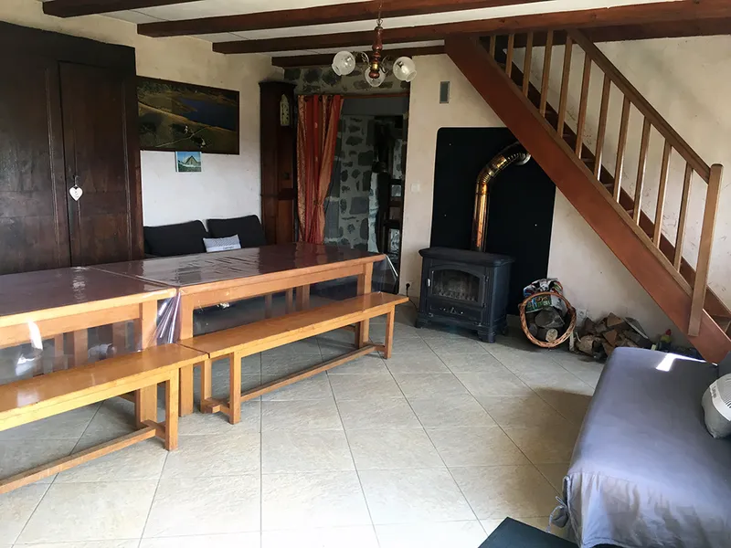 Grand séjour avec longue table en bois et bancs pour le groupe, poêle à bois et escalier