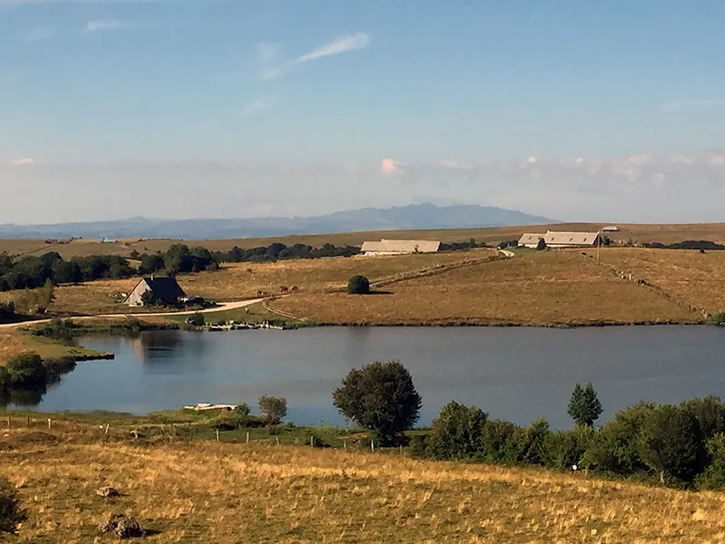 Vue panoramique sur le lac d'altitude bordé de prairies et de collines cantaliennes
