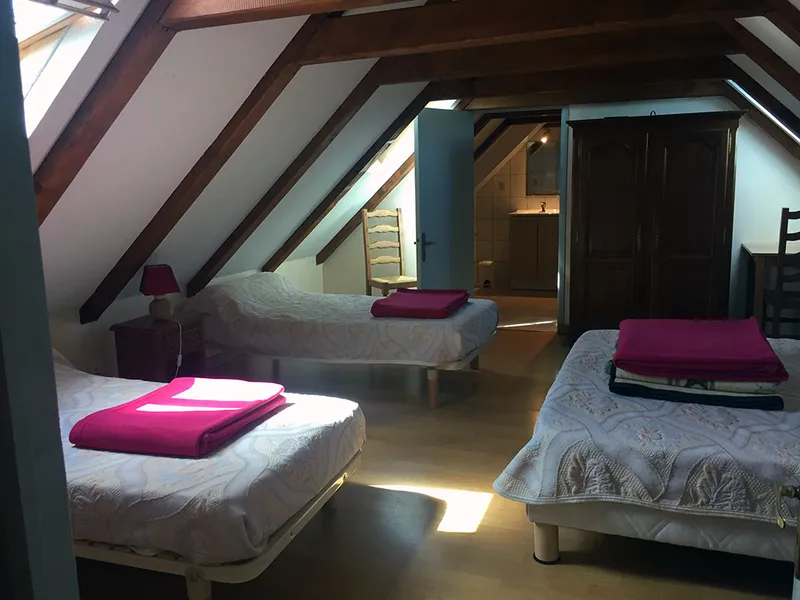 Chambre mansardée avec trois lits simples séparés par des poutres apparentes en charpente